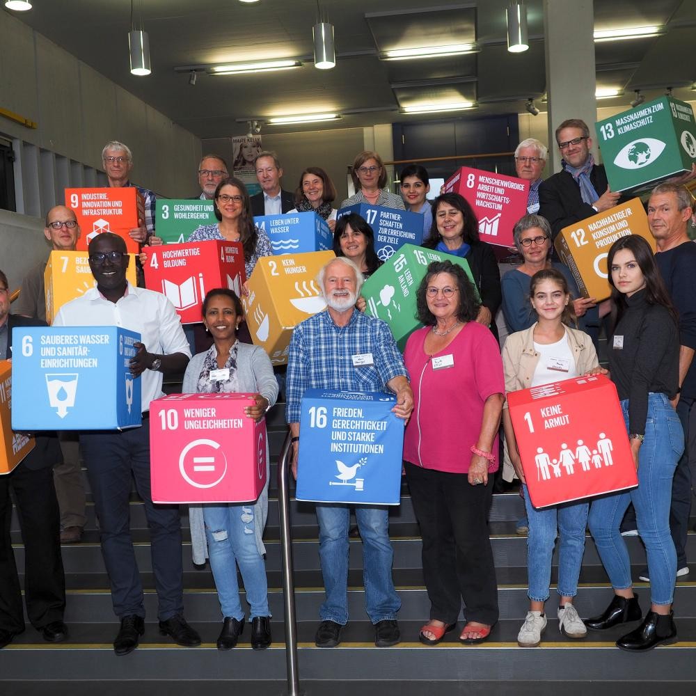 Eine Gruppe Menschen, die die Sustainable Development Goals, symbolisch auf Würfel gedruckt, in den Händen hält