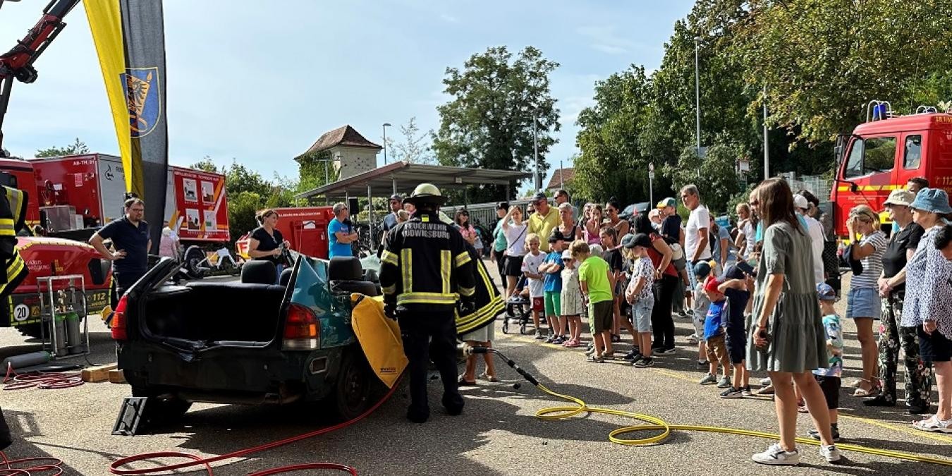 Bei einer Vorführung im Rahmen des Tags der offenen Tür stehen Feuerwehrleute rund um ein demoliertes Auto. Mehrere Zuschauer beobachten die Aufführung.