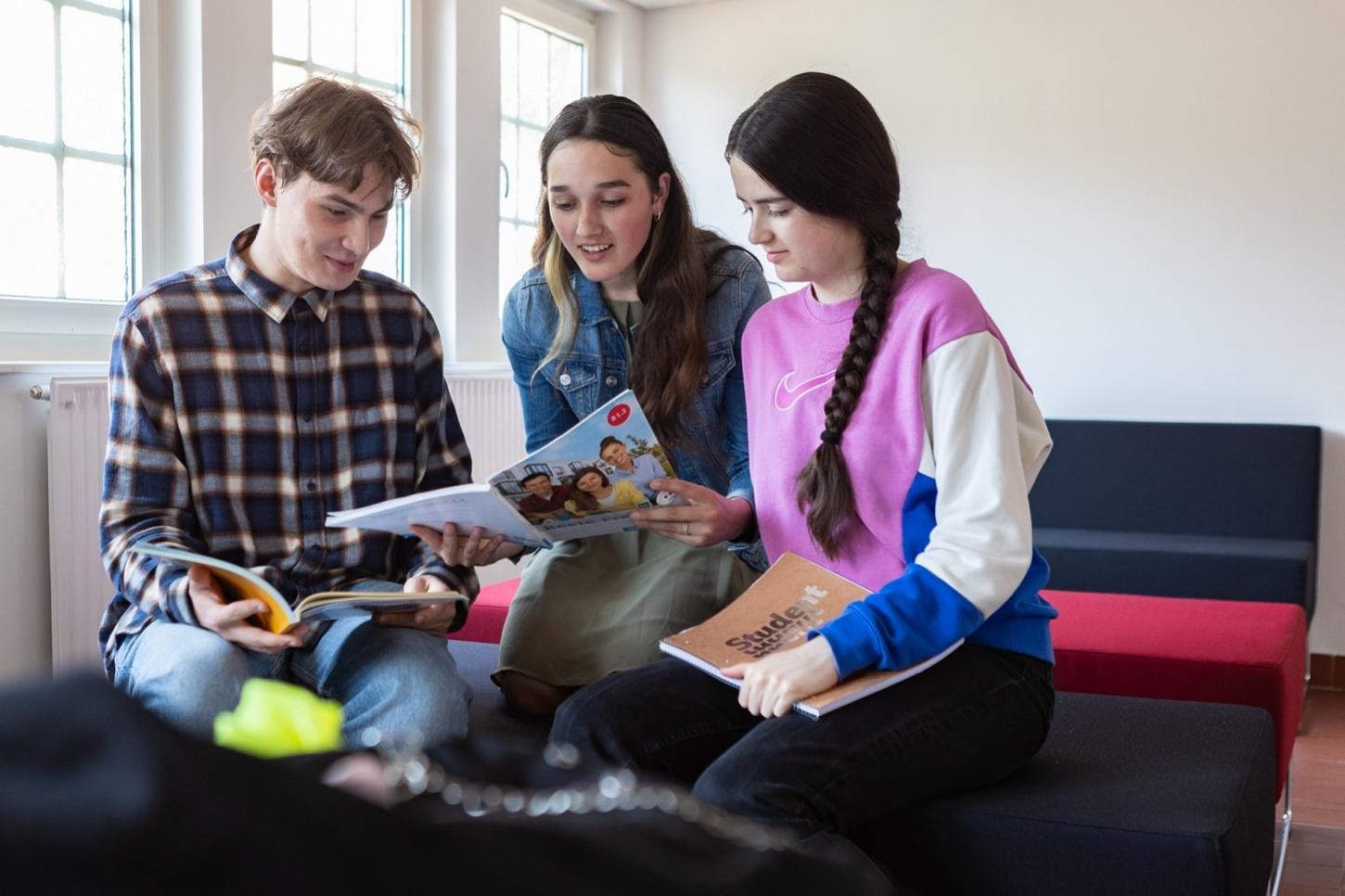 Drei Personen sitzen auf einer Couch und lesen Bücher oder Magazine.