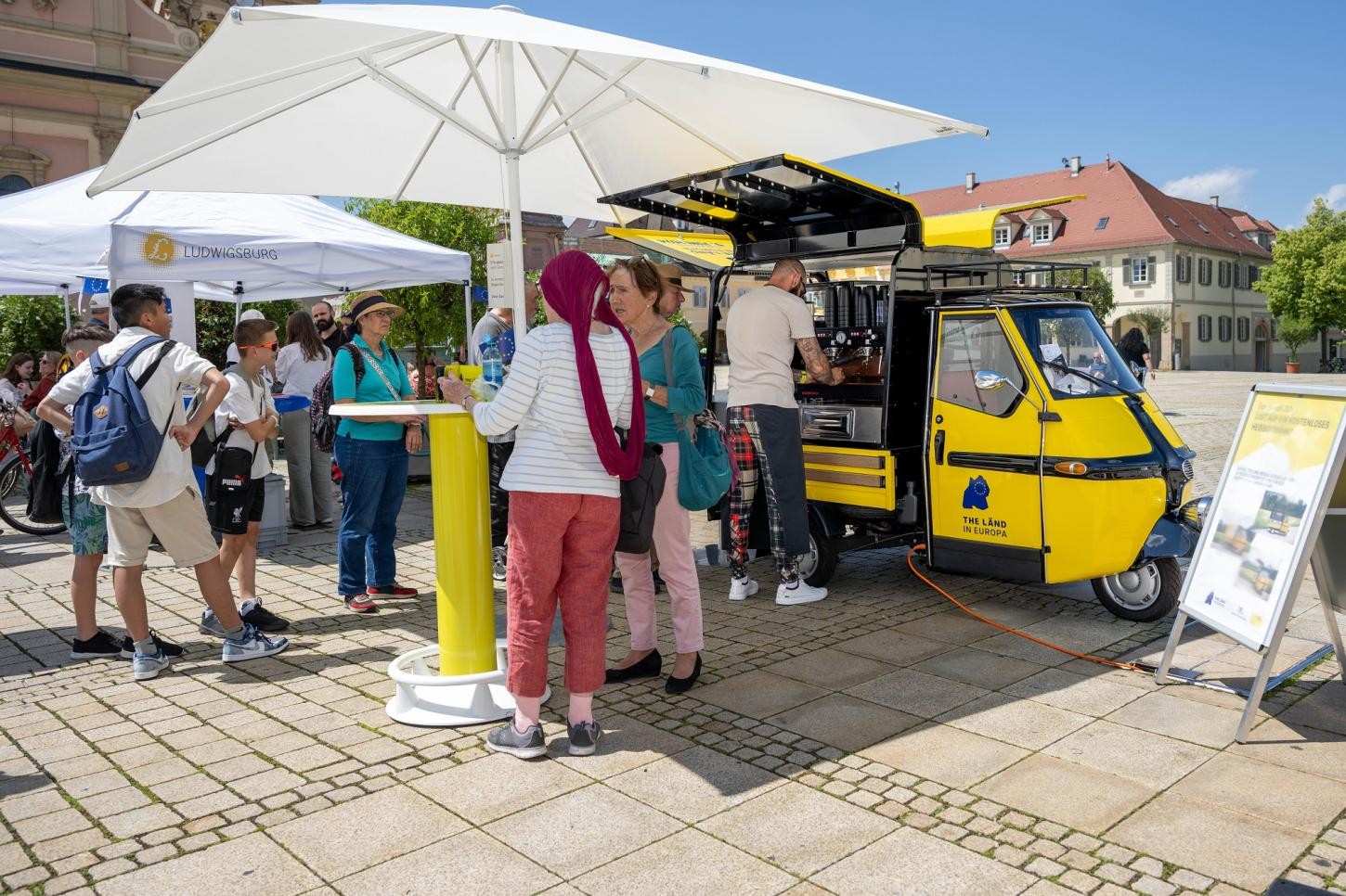 Personen am Stand The Länd mit Sonnenschirm