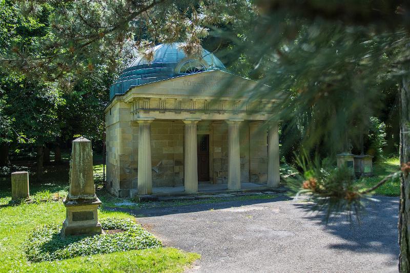 Blick auf eine Friedhofsgruft, etwas hinter Blättern versteckt.