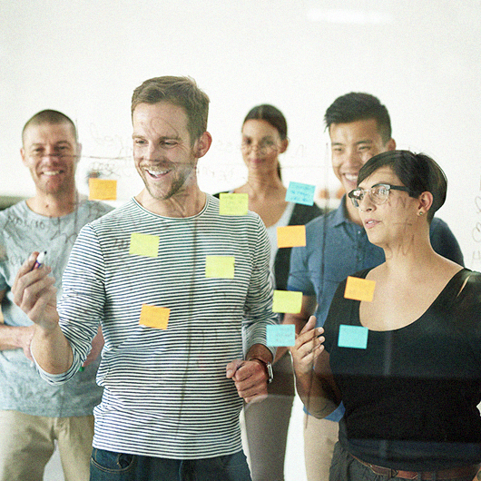 Klimaschutz in Unternehmen junge Menschen kleben Post-its an eine Glasscheibe