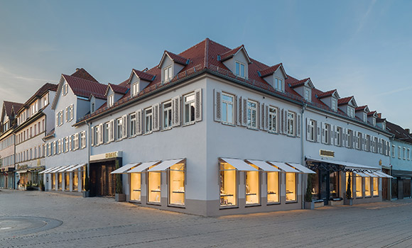 Gebäudeansicht des Eckhauses der Firma Hunke. Die Fensterläden sind erleuchtet