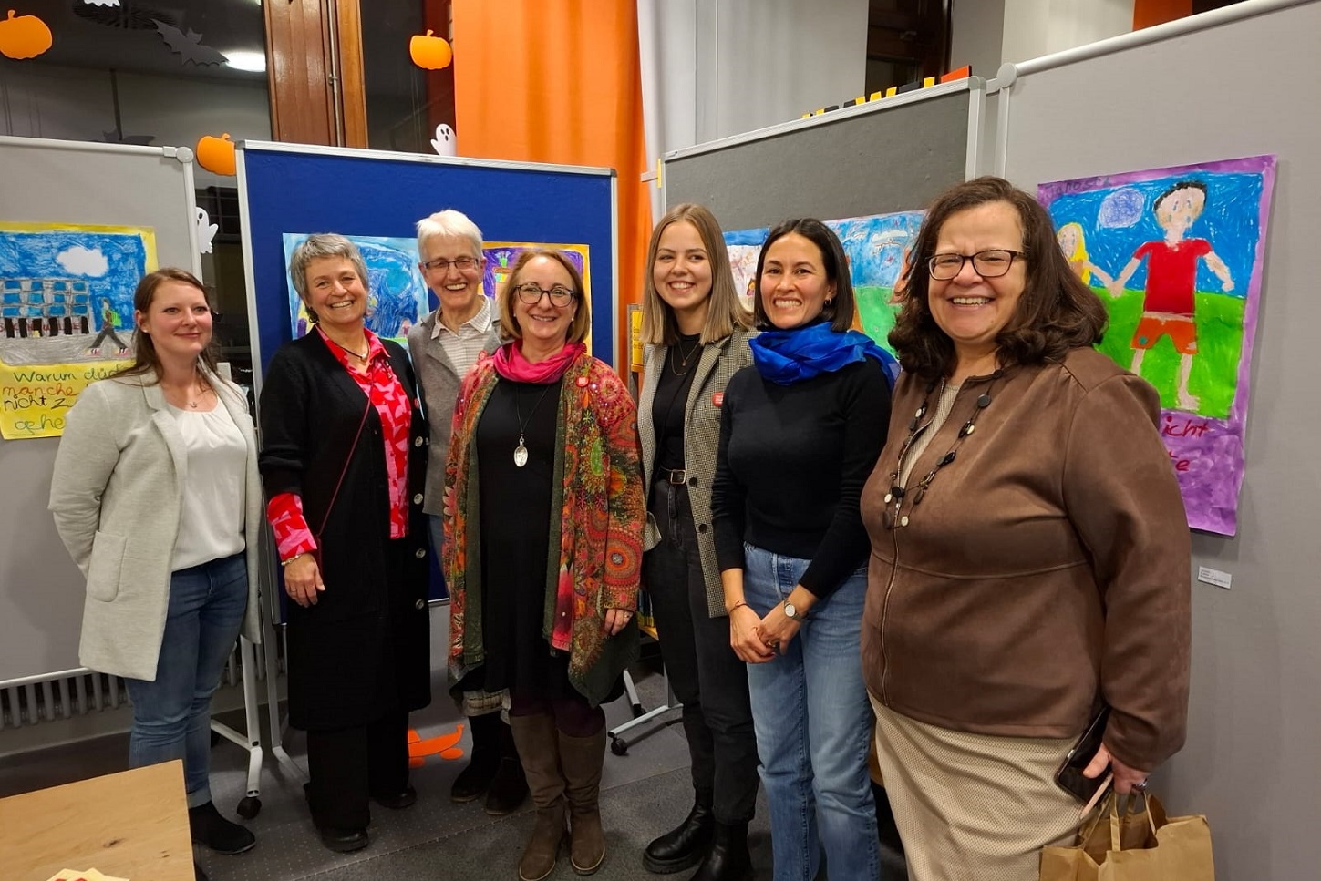 Frau Schmetz steht gemeinsam mit weiteren Akteurinnen vor den gemalten Bildern.