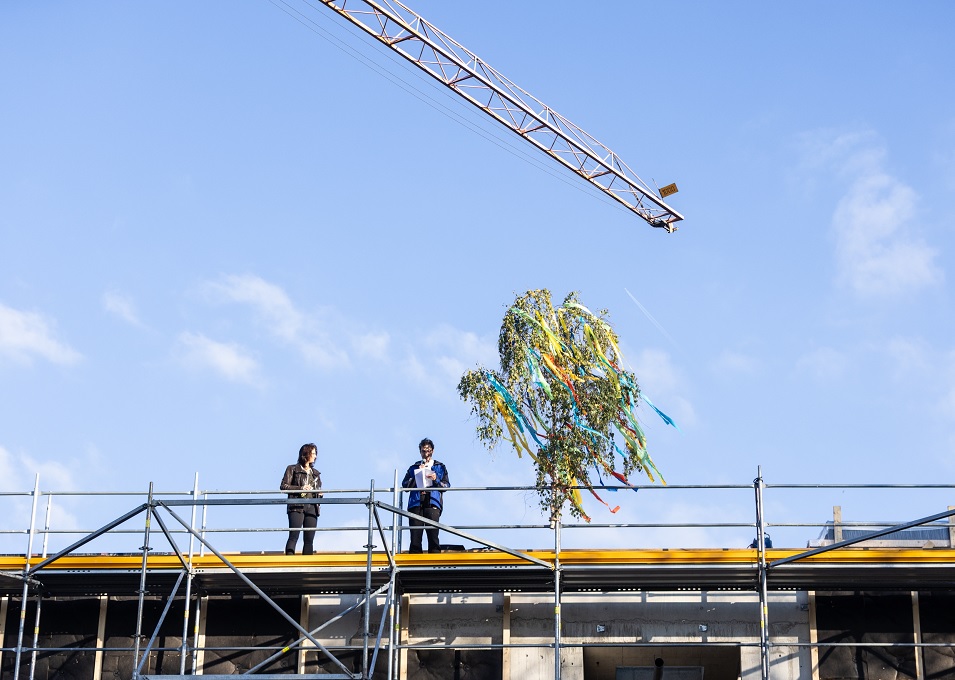 Richtfest_Oststadthalle_Richtspruch Baubürgermeisterin Andrea Schwarz und Zimmermann Frank Grottenmüller stehen auf dem Dach der Oststadthalle. Neben ihnen hängt die Richtkrone.