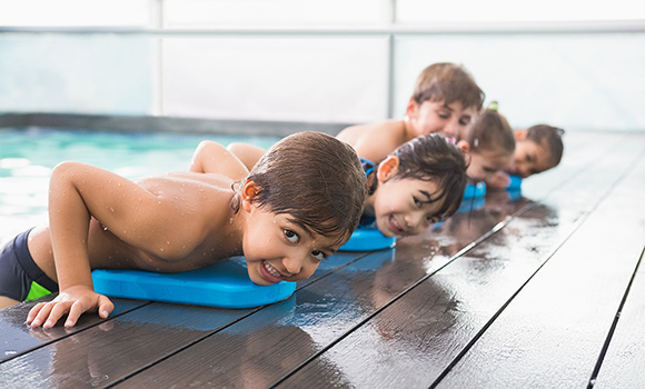 Fünf Kinder mit einem Schwimmbrett am Beckenrand.
