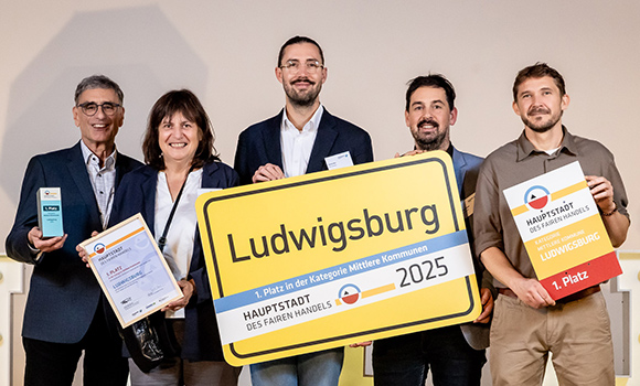 Die fünf Geehrten halten Urkunden und ein Ortsschild "Ludwigsburg" mit der Aufschrift "Hauptstadt des Fairen Handels 2025" in der Hand