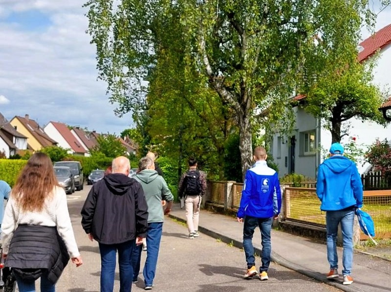 Personen spazieren auf einer Straße an Häusern vorbei