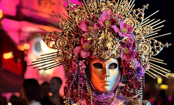 Portrait-Aufnahme eines Kostümträgers mit einem aufwändigen Kopfschmuck und goldener Maske
