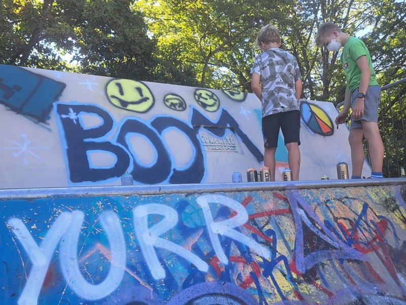Zwei Jungen mit Atemschutzmaske sprühen bunte Wand vom Skatepark