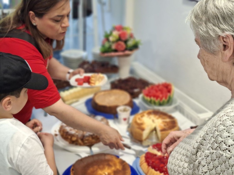 Frau schneidet Kuchen vom Kuchenbuffet, ältere Dame und Kind schauen zu