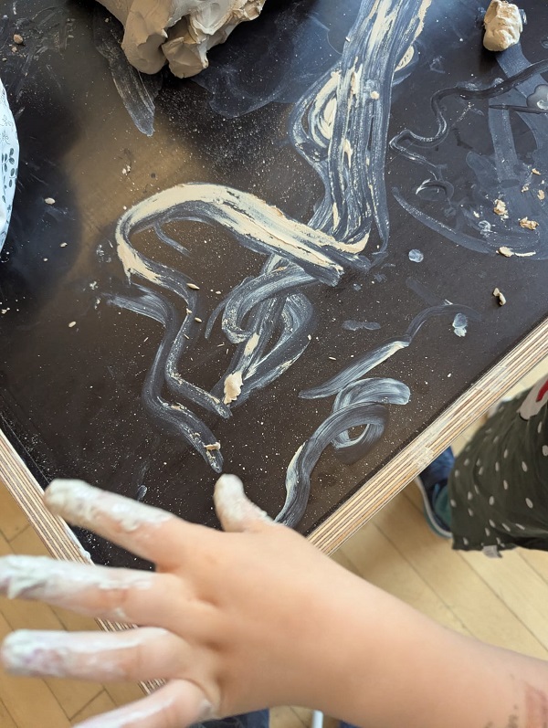 Kinder zeichnen mit Tonschlick auf einem dunklen Tisch Kunstwerke