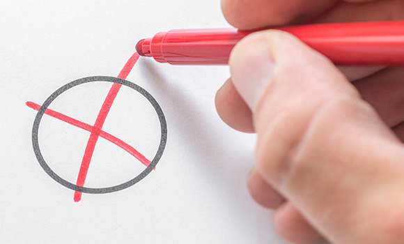 Hand mit rotem Stift setzt ein Kreuz in einen leeren Kreis.