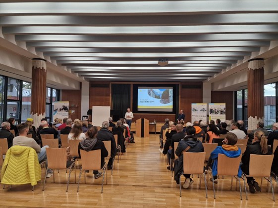 Personen sitzen in Reihen im Saal und hören Vortrag zu