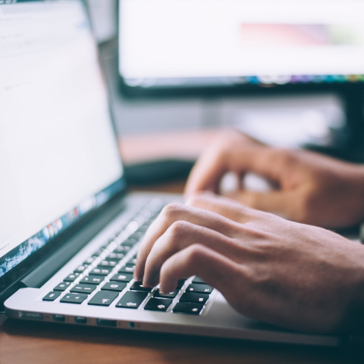 Hände, die auf der Tastatur eines MacBooks tippen.