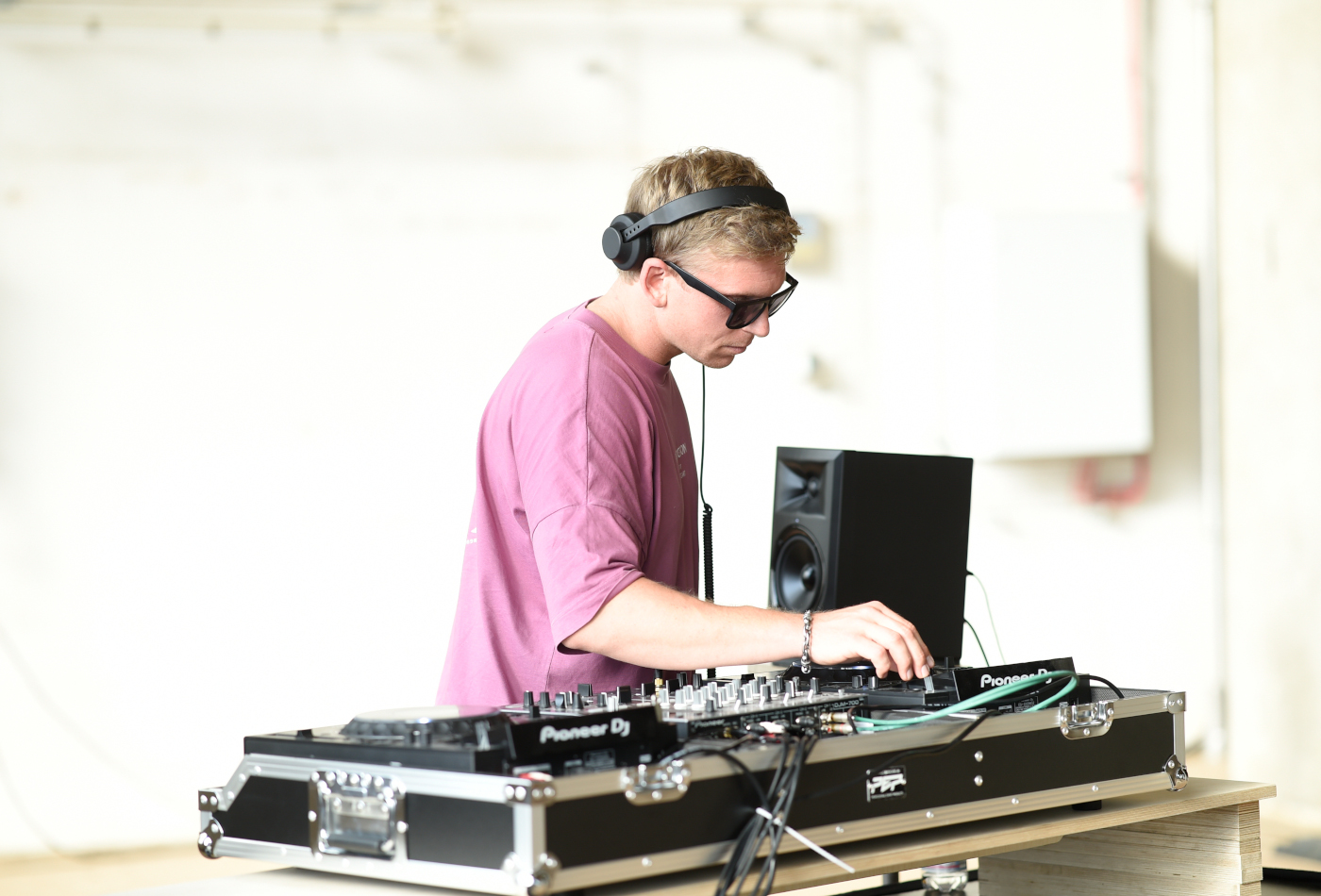 Ein DJ mit lila T-Shirt steht an einem Mischpult und spielt Musik.