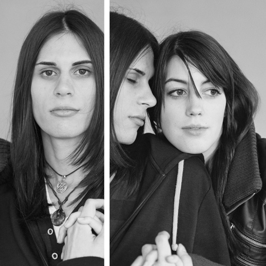 Die schwarz-weiß Fotografie ist zweigeteilt und zeigt zwei junge Frauen, die sich im Arm halten. 