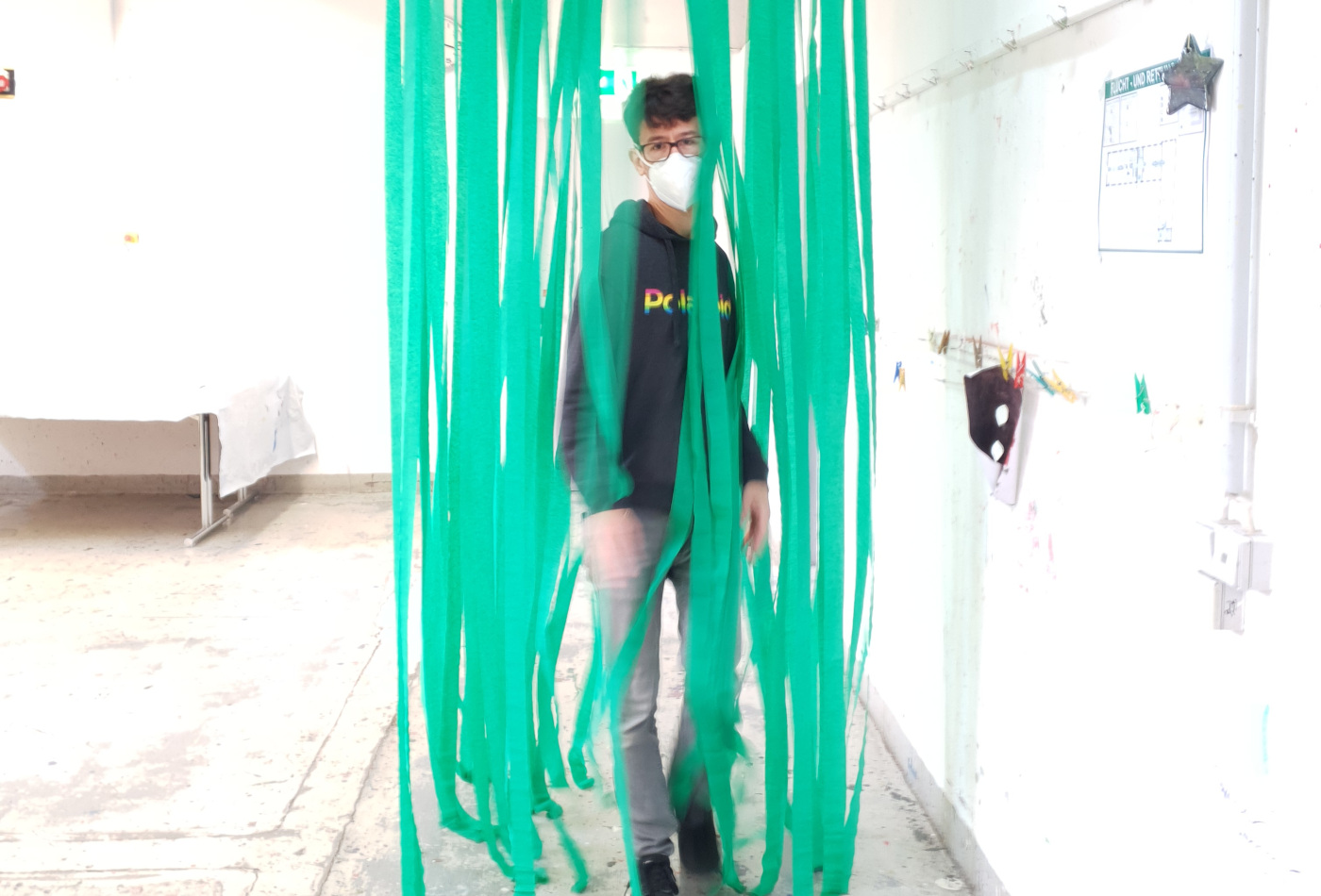 Ein junger Mann durchschreitet einen Vorhang aus grünen Krepp-Streifen.