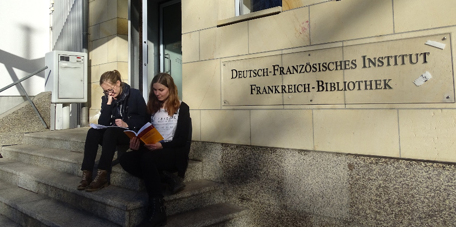  Zwei junge Frauen sitzen auf den Stufen zum Eingang des Deutsch-Französischen Institutes 