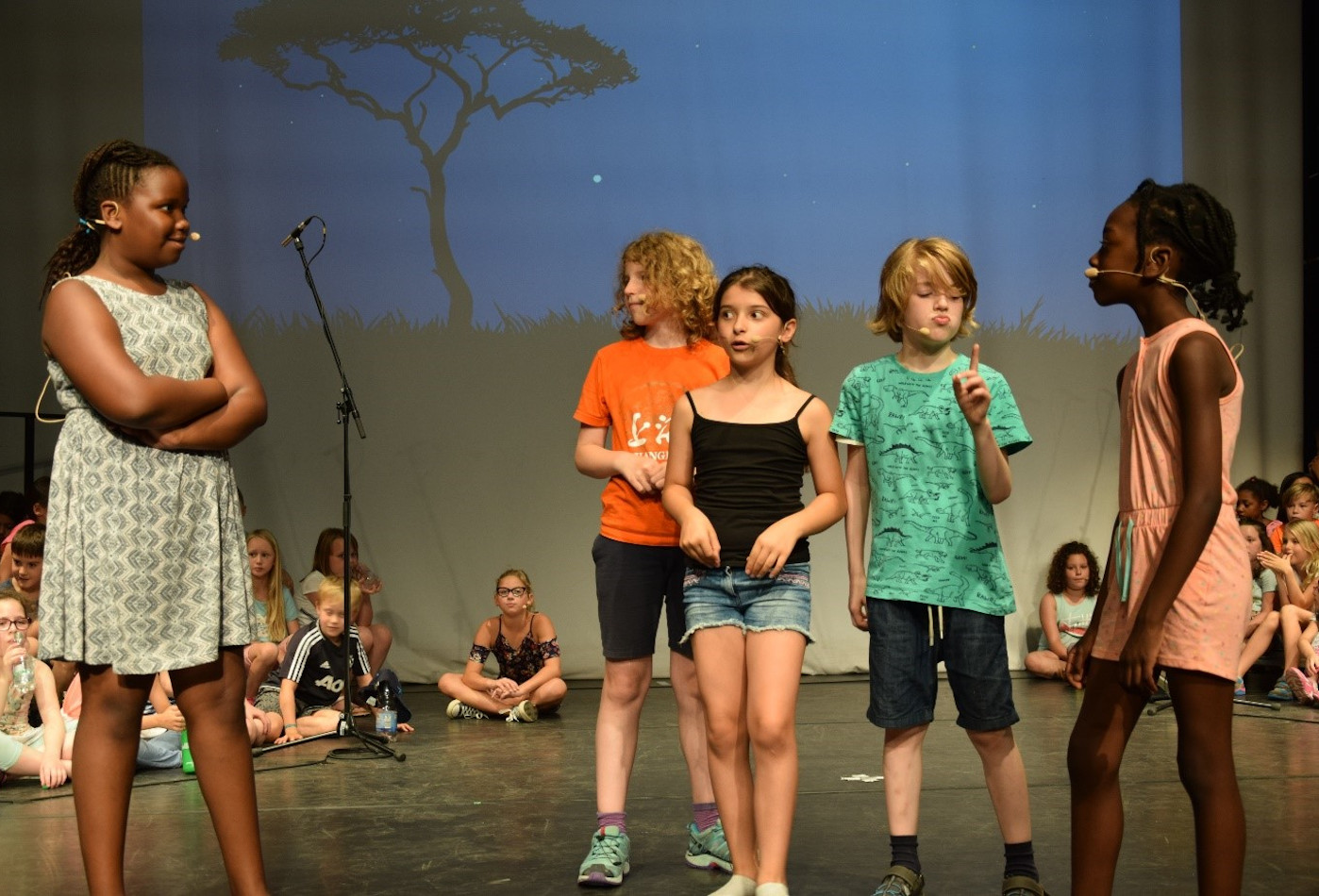 Fünf Kinder stehe auf einer Bühne und führen ein Musikstück auf.