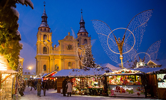 Weihnachtsmarktstände vor Kirche und großen Engelfiguren.