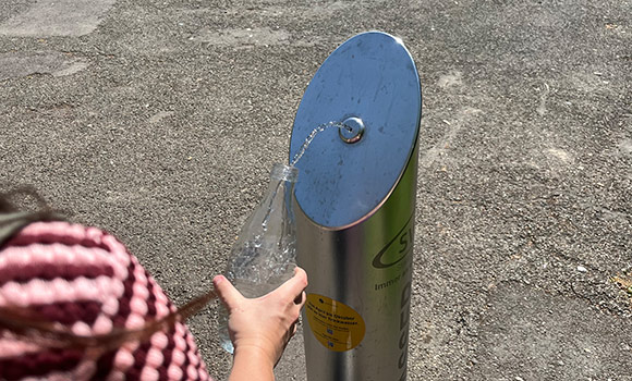 Hand hält Wasserflasche an einen Trinkbrunnen.