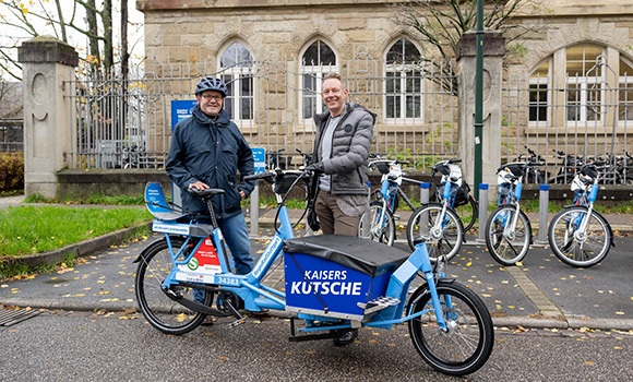 Matthias Knobloch und Bürgermeister Sebastian Mannl stehen hinter einem Lastenpedelec, auf dem der Name "Kaisers Kutsche" steht.