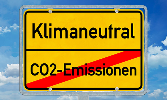 Ortsschild mit folgenden Aufschriften: oben das Wort "Klimaneutral". Unten das durchgestrichene Wort "CO2-Emissionen".