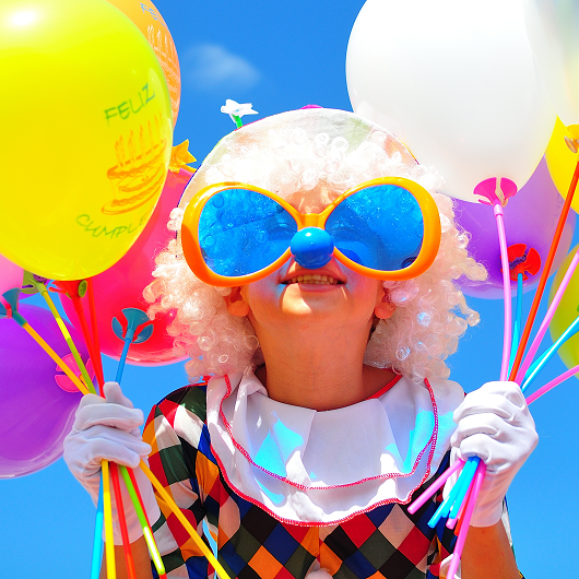 lächelnder Clown mit Ballons und großer Sonnenbrille mit hellblauen Gläsern