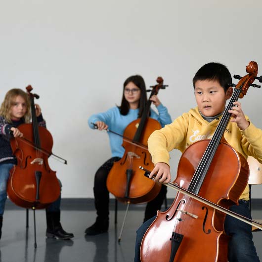 Ein Junge und zwei Mädchen spielen Cello.