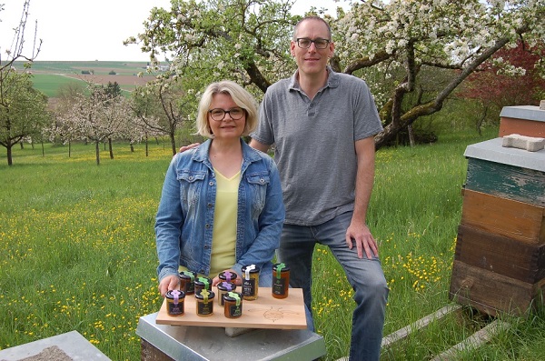 Herr und Frau Deckert mit Honiggläsern neben Bienenstöcken 