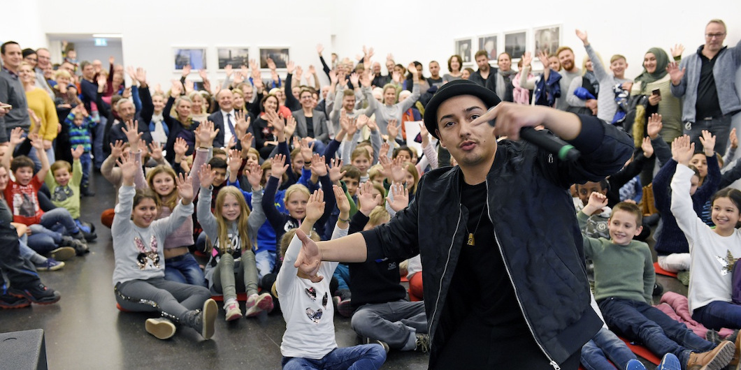 Ein junger Beatboxer steht vor einer großen Menschenmenge, die winkt.