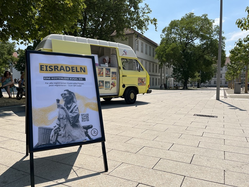 Infoständer mit Titel Eisradeln vor Eiswagen auf sonnigem Arsenalplatz