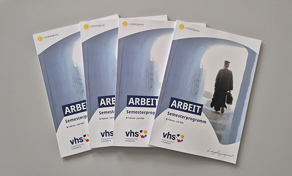Vier Programmhefte legen nebeneinander. Auf der Titelseite steht das Wort "Arbeit".