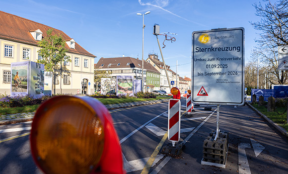 Baustellenschild an einer Straße mit der Aufschrift: Sternkreuzung - Umbau zum Kreisverkehr 1.9.2025 bis September 2026. Im Hintergrund Sternkreuzung mit mit Schlangen-Skulptur