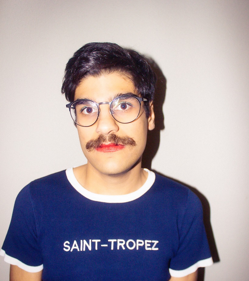 Ein Mann mit Brille und blauem T-Shirt mit der Schrift Saint-Tropez blickt in die Kamera.