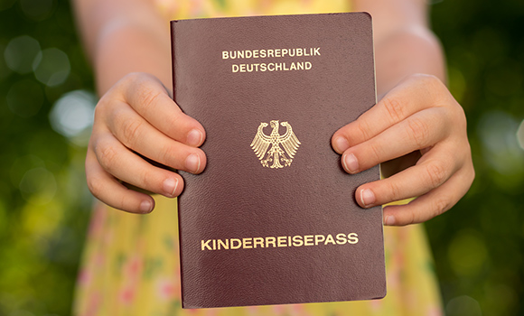 Mädchen hält Kinderreisepass in die Kamera.