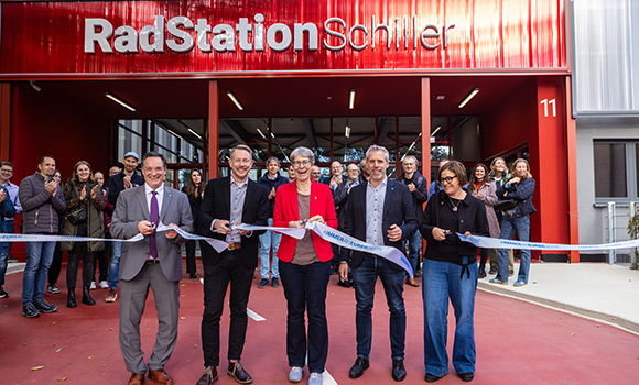 Fünf Personen schneiden ein Band durch. Im Hintergrund die Radstation Schiller.