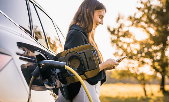 Frau steht neben Elektroauto, das gerade geladen wird.