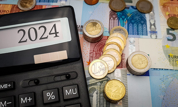 Auf dem Display eines Taschenrechners steht die Jahreszahl 2024. Neben dem Taschenrechner liegen Euro-Scheine und -Münzen.
