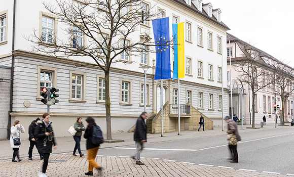 An zwei Fahnenmasten vor dem Rathaus hängen die ukrainische Flagge (in blau und gelb) und die Flagge der Europäischen Union.