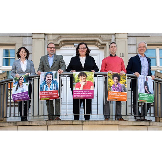 Fünf Personen auf einem Balkon halten Plakate mit Informationen zu Stellenangeboten in Kitas. In der Mitte steht die Erste Bürgermeisterin Renate Schmetz.