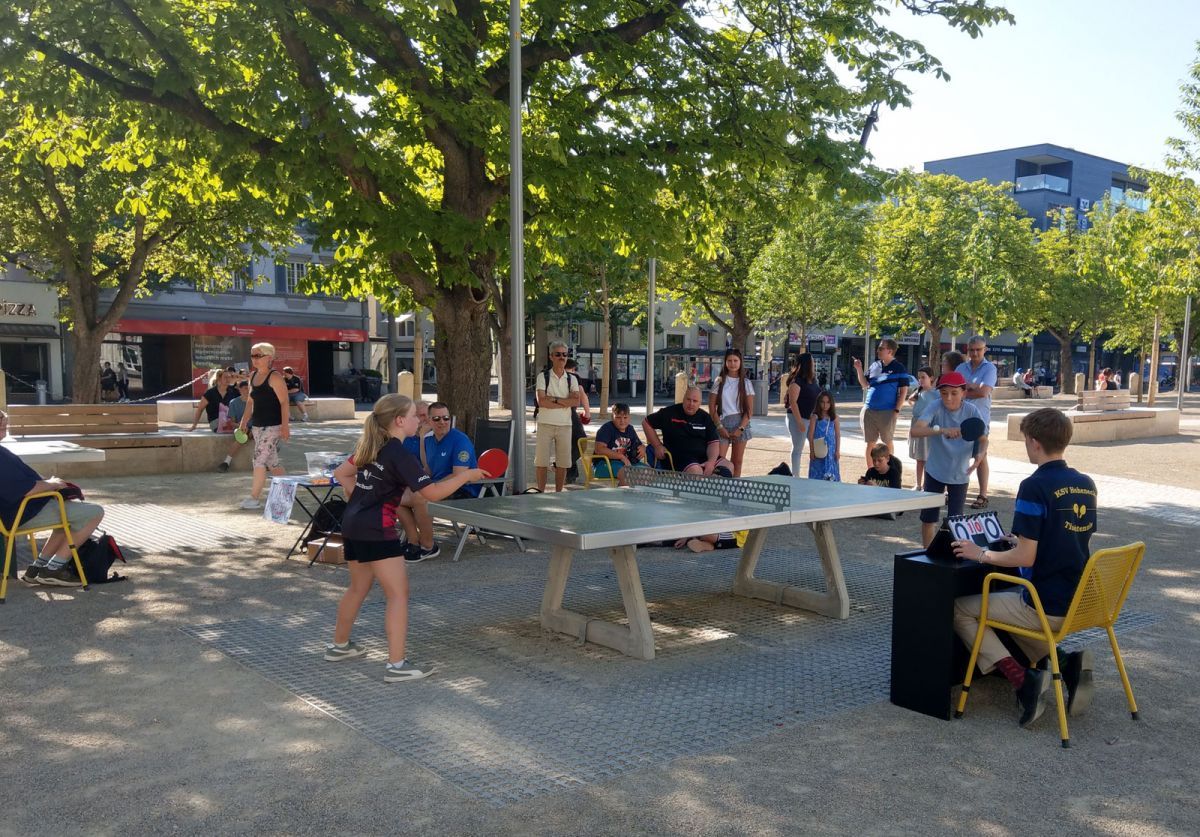Junge Personen spielen Tischtennis, Personen schauen gebannt zu