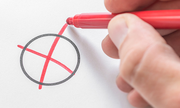 Hand setzt mit einem Stift ein Kreuz in einen Kreis.