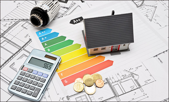 Auf einer Unterlage liegen Baupläne, das Modell eines Hauses, ein Taschenrechner, Kleingeld sowie ein Heizungsregler und eine Abbildung mit Energieeffizienzklassen.