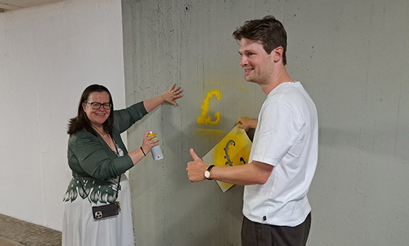 Erste Bürgermeisterin Renate Schmetz hält eine Spraydose in der Hand, der Sprayer Tim Scheu eine Schablone mit dem Ludwigsburg-L. An die Wand  ist ein gelbes L gesprüht.