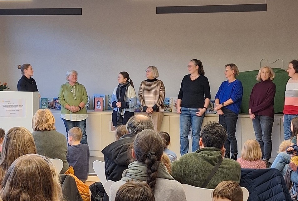 Sieben Frauen stehen nebeneinander. Davor befindet sich das Publikum mit Erwachsenen und Kindern.