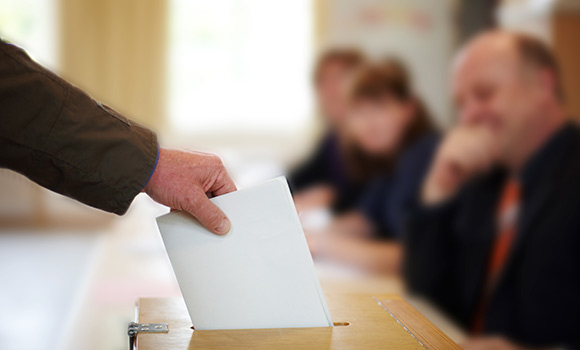 Stimmzettel wird in Wahlurne gesteckt.