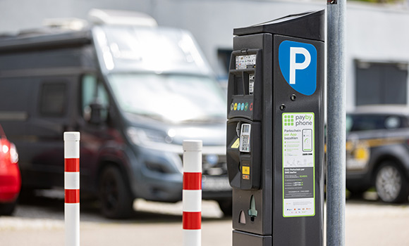 Parkscheinautomat mit Autos im Hintergrund.