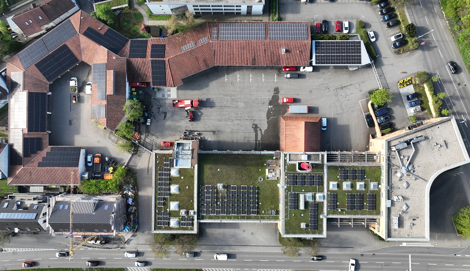 Luftaufnahme der Photovoltaikanlagen auf dem Flachdach der Hauptfeuerwache, dem Satteldach des benachbarten TDL-Gebäudes und einer Containerbedachung auf dem Hof der Feuerwehr.  